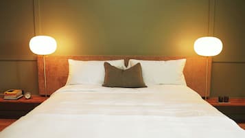 A neatly made bed with white and brown pillows, two bedside lamps, a nightstand with a book and a clock, and a wooden headboard.