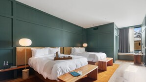 A modern hotel room with two beds, bedside lamps, a wooden bench, a small table, and a window with curtains. - Albert Hotel (Fredericksburg)