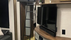 Ett kompakt bostadsutrymme med en TV, träskåp, en stege och ett litet bord.