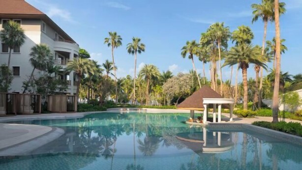 Piscina de resort con palmeras y un pabellón.