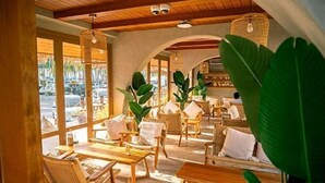 Un rincón interior acogedor con mobiliario de mimbre, ventanas amplias y plantas tropicales.