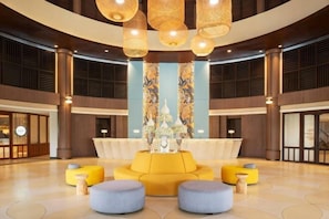 Un hall d’entrée spacieux avec un espace salon central, de grandes fenêtres et un lustre moderne.