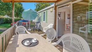 A covered patio with a table set for two, outdoor chairs, and a car parked in the background. - Awesome (sta)caravan in Saint-Georges-de-Didon (Saint-Georges-de-Didon)