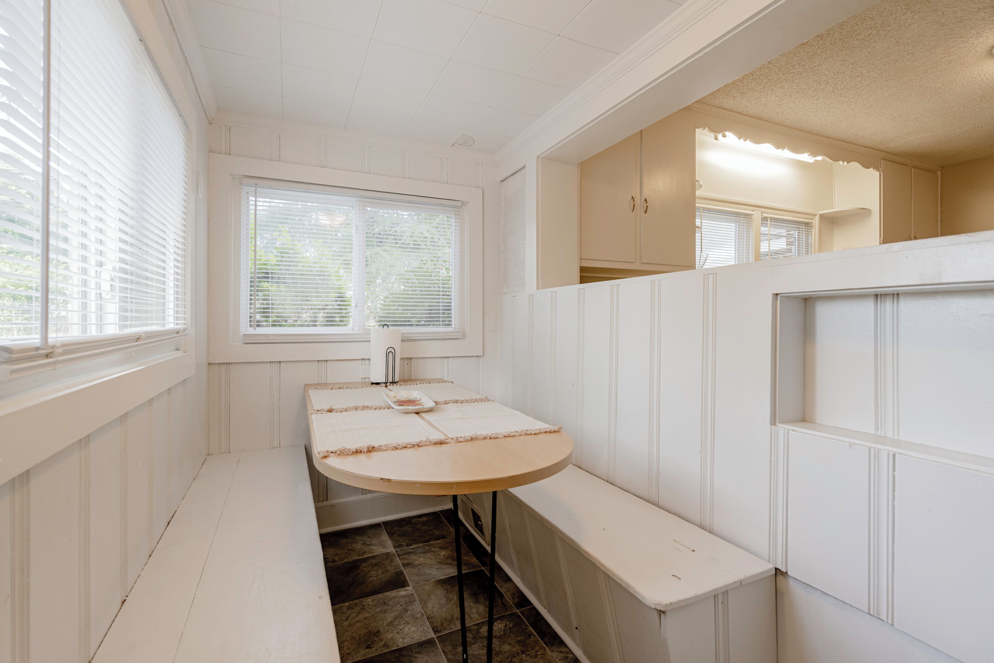 A compact kitchen with a round table, bench seating, and a window with blinds.
