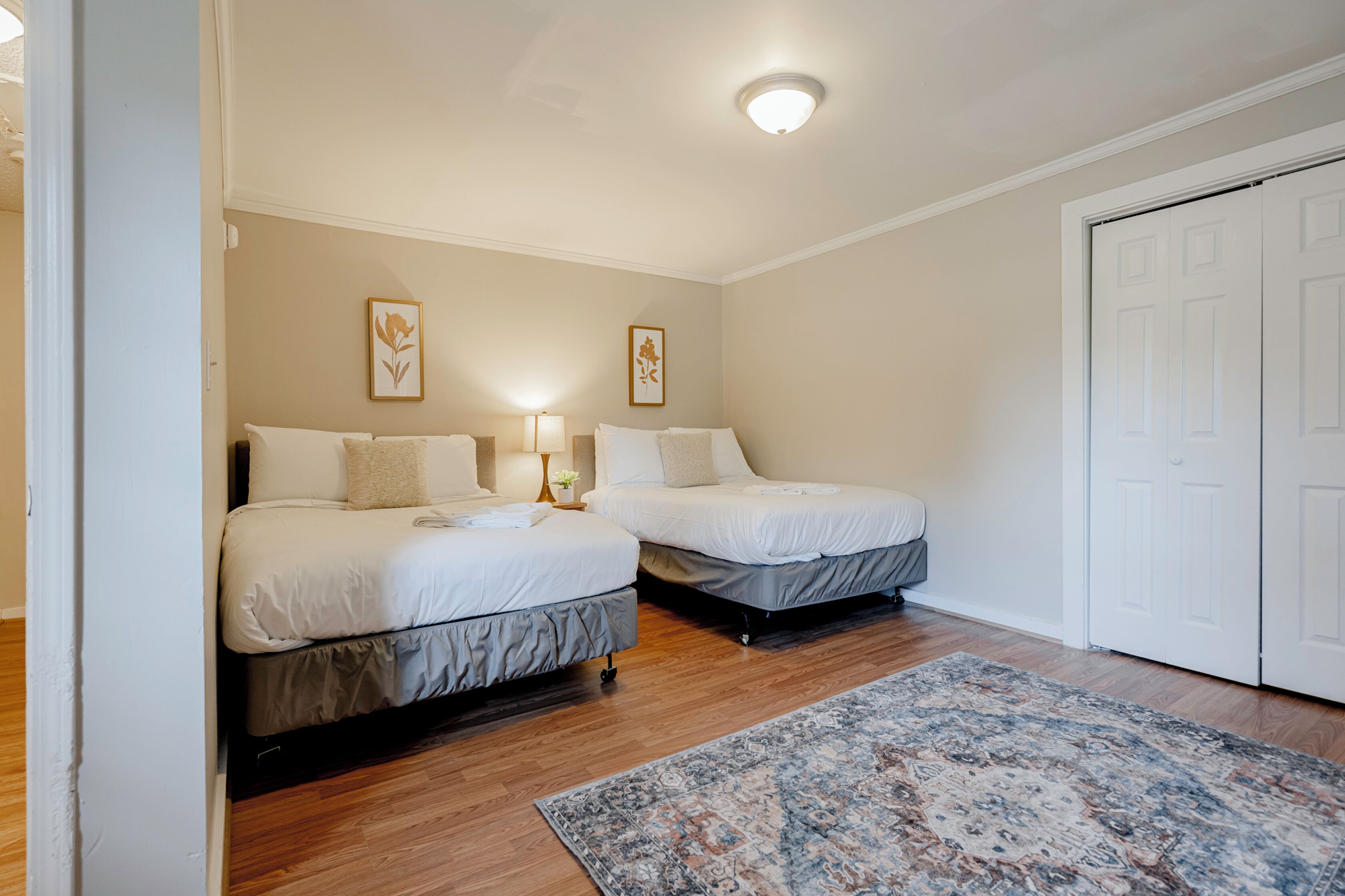 Un dormitorio con dos camas, piso de madera, alfombra estampada y una puerta blanca.