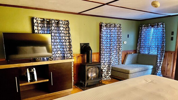 Habitación de hotel con cama, televisor, cafetera, chimenea y cortinas estampadas.