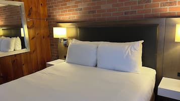 A hotel room with a brick wall, a large bed with white linens, a wooden headboard, and two bedside lamps.