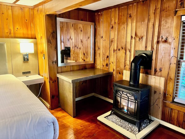 L’intérieur d’un chalet en bois comprend un lit, un bureau en bois, un miroir et un poêle à bois.