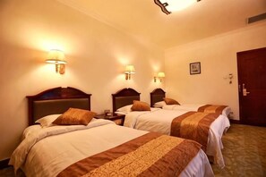 Una habitación de hotel con tres camas, cada una con cabecera y lámparas de noche.