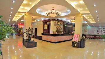 A hotel lobby with a reception desk, a chandelier, and a large plant.