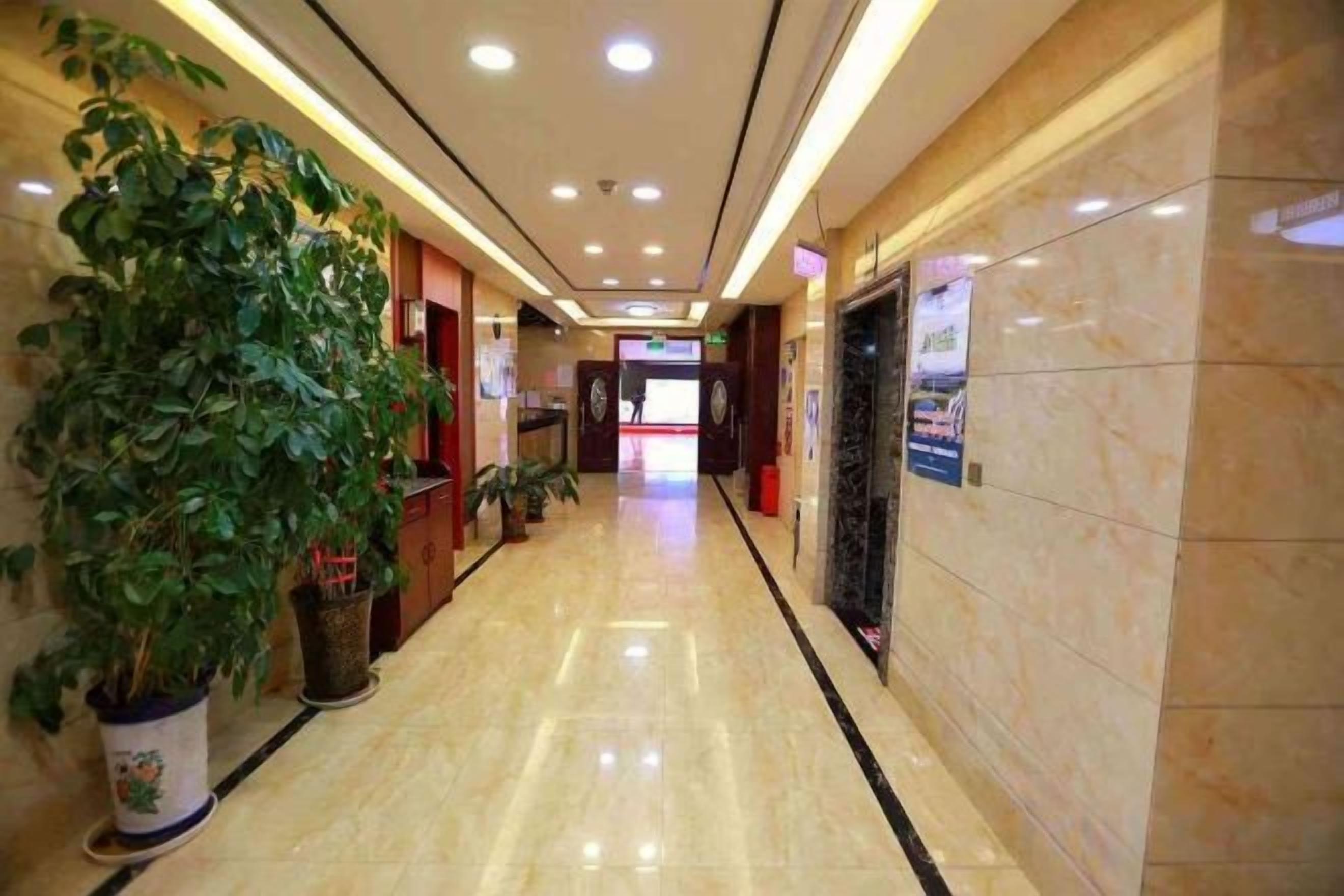 Un pasillo de hotel con piso pulido, plantas en macetas y un mostrador de recepción.