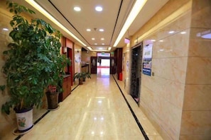 Un pasillo de hotel con piso pulido, plantas en macetas y un mostrador de recepción.