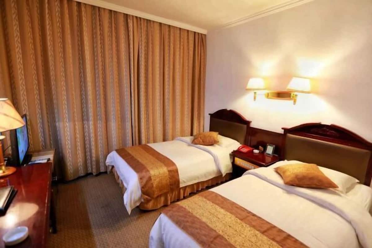 Una habitación de hotel con dos camas, un escritorio con lámpara y un televisor.