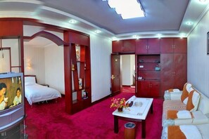 A hotel room with a bed, a sofa, a coffee table, and a TV. - Dong Fang Hotel (Jiayuguan)