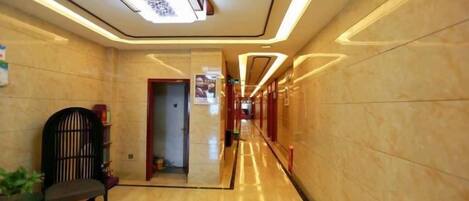 A hotel corridor with a marble floor, a reception desk, and a door leading to another room.