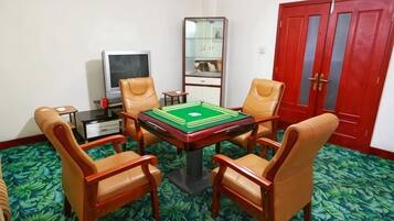 A room with a green carpet, a table with a green and white board game, four leather chairs, a television, and a red wardrobe.