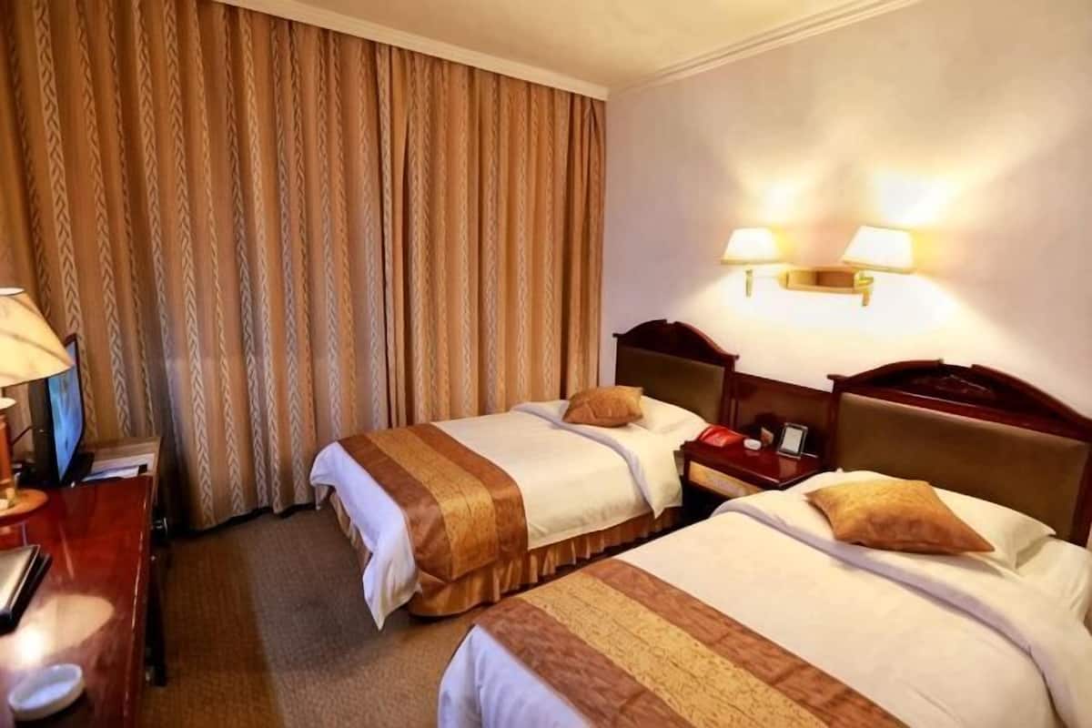 Habitación de hotel con dos camas, un escritorio, un televisor y una cortina.