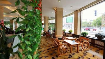 A hotel lobby with a patterned carpet, wooden furniture, and large windows offering a view of the street.