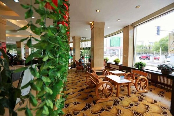 A hotel lobby with a patterned carpet, wooden furniture, and large windows offering a view of the street. - Dong Fang Hotel (Jiayuguan)