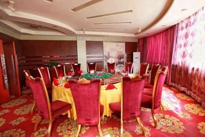 A dining area with round tables, red upholstered chairs, and a red carpeted floor. - Dong Fang Hotel (Jiayuguan)