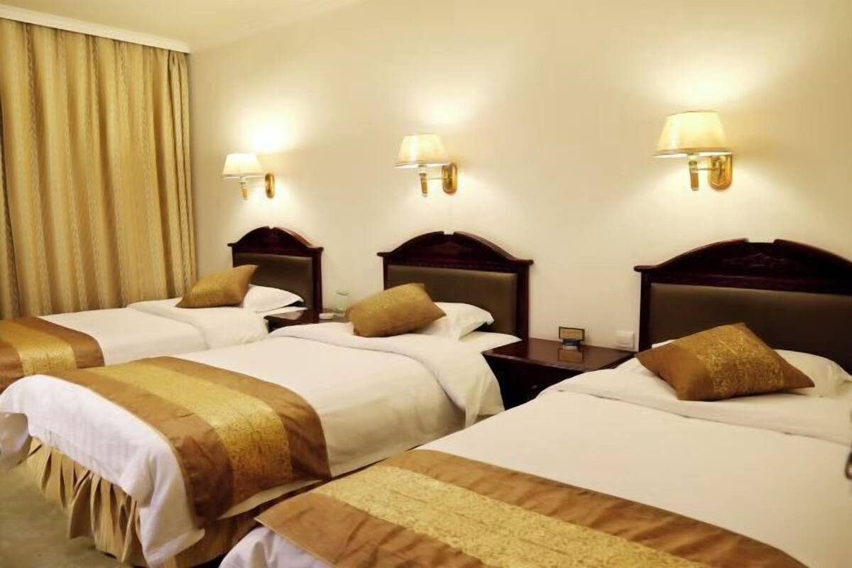 Habitación de hotel con dos camas, cada una con cabecera, mesitas de noche, lámparas y cortina.