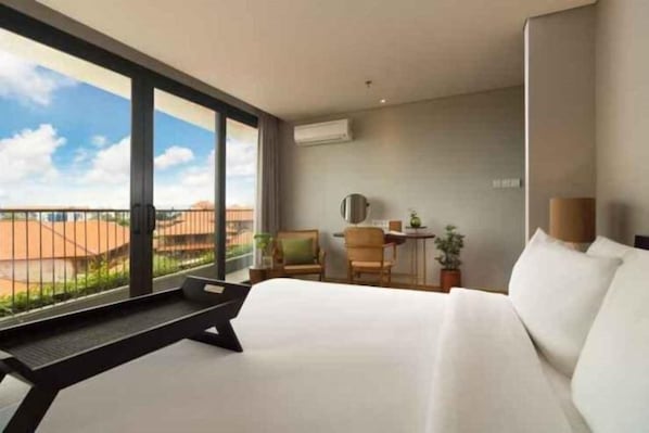 Una camera d'albergo con un letto grande, una scrivania, due sedie, un tavolino e vista sul paesaggio attraverso ampie finestre.