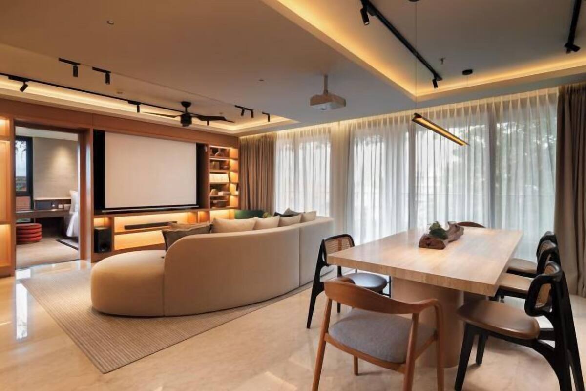 A modern living room with a curved sofa, a dining table, and a projector screen.