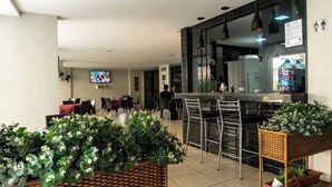 Un restaurant moderne doté d’un bar, de différents espaces pour s’asseoir et d’un écran de télévision.