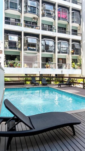 Una piscina al aire libre, sombrillas, sillones reclinables de piscina