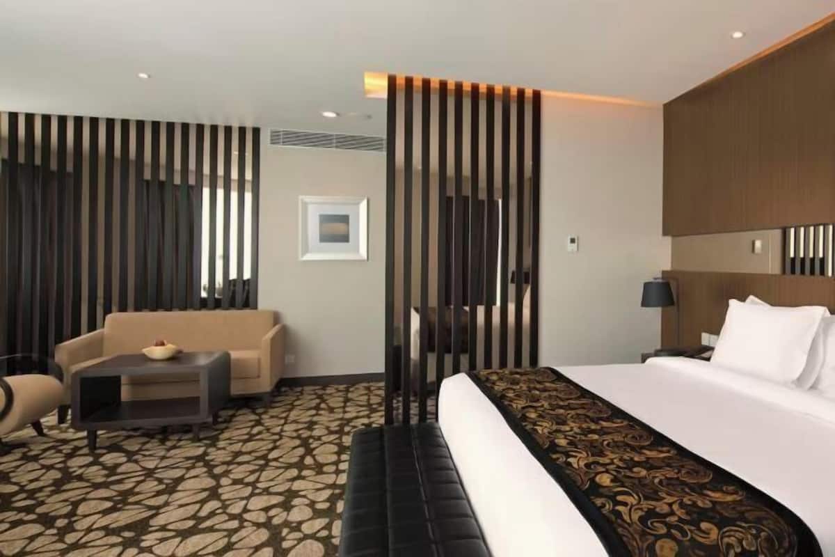 Una habitación de hotel con cama, sofá, una mesita y un separador decorativo.