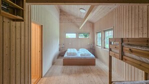 Interior de una cabaña de madera con una cama central, dos mesitas de noche y una litera a la derecha.