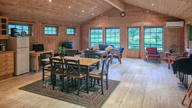 Una cabaña amplia con paredes y techo de madera, un comedor con mesa y sillas, un sofá y una cocina con electrodomésticos.