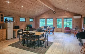 Une cabine spacieuse aux murs et au plafond en bois, un coin repas avec une table et des chaises, un canapé et un coin cuisine équipé d’appareils électroménagers.