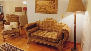 Een woonkamer met een vintage bank, een houten stoel, een rode lamp en een ingelijst kunstwerk aan de muur.