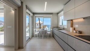 A modern kitchen with a view of the sea, a dining area with a table and chairs, and a large window.