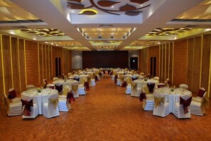 A banquet hall with round tables, white tablecloths, and chairs with red cushions. - Ramada Resort Cochin (Kochi)