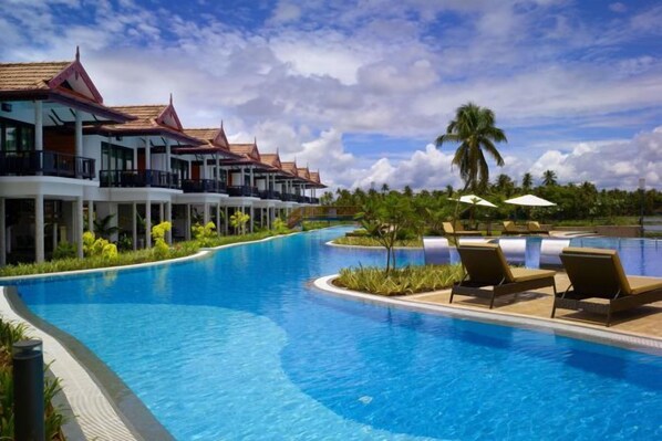A swimming pool with lounge chairs, a palm tree, and a building with a red roof. - Ramada Resort Cochin (Kochi)
