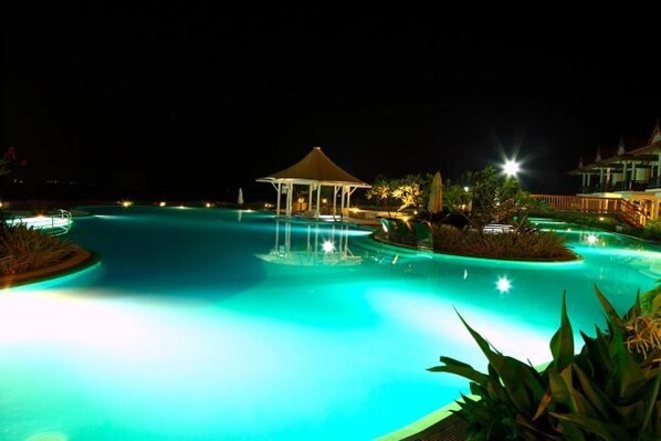 A nighttime view of a swimming pool with a gazebo and surrounding tropical plants.