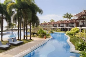 A swimming pool with lounge chairs, palm trees, and resort buildings. - Ramada Resort Cochin (Kochi)