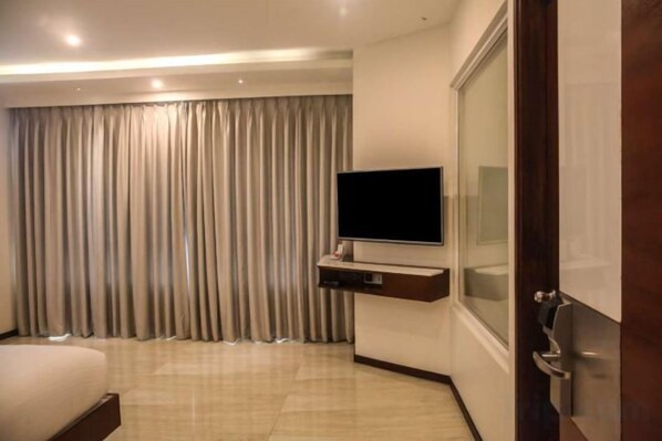 A hotel room with a bed, a flat-screen TV mounted on the wall, and a large window with curtains. - Ramada Resort Cochin (Kochi)