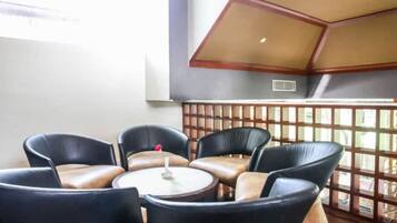 A seating area with leather chairs and a small table, a wooden partition, and a view through a lattice window.