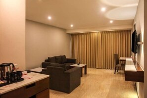 A hotel room with a sofa, a small table, a TV mounted on the wall, and a curtain-covered window. - Ramada Resort Cochin (Kochi)