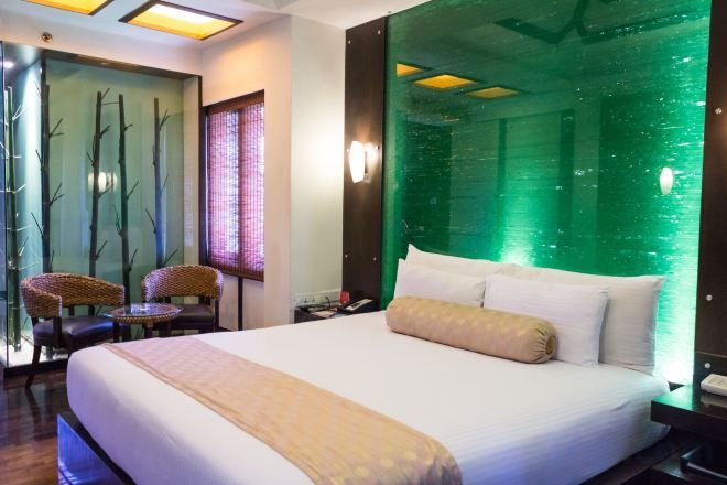 A hotel room with a large bed, a green wall feature, a small table, and two chairs.