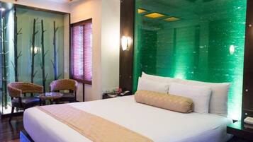 A hotel room with a large bed, a green wall feature, a small table, and two chairs.