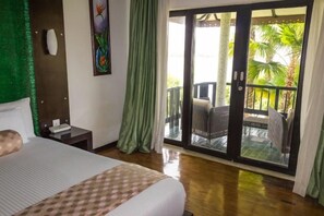 A hotel room with a bed, a nightstand, a painting, a sliding glass door to a balcony with chairs, and a view of palm trees. - Ramada Resort Cochin (Kochi)