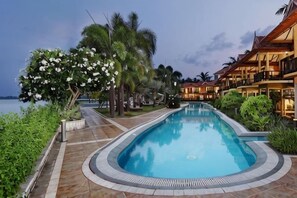 A swimming pool with a curved edge, surrounded by a wooden deck and palm trees. - Ramada Resort Cochin (Kochi)