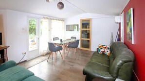 Ein Wohnzimmer mit einem grünen Sofa, einem Esstisch mit Stühlen, einer roten Wand und einem durch eine Glastür einsehbaren Küchenbereich.