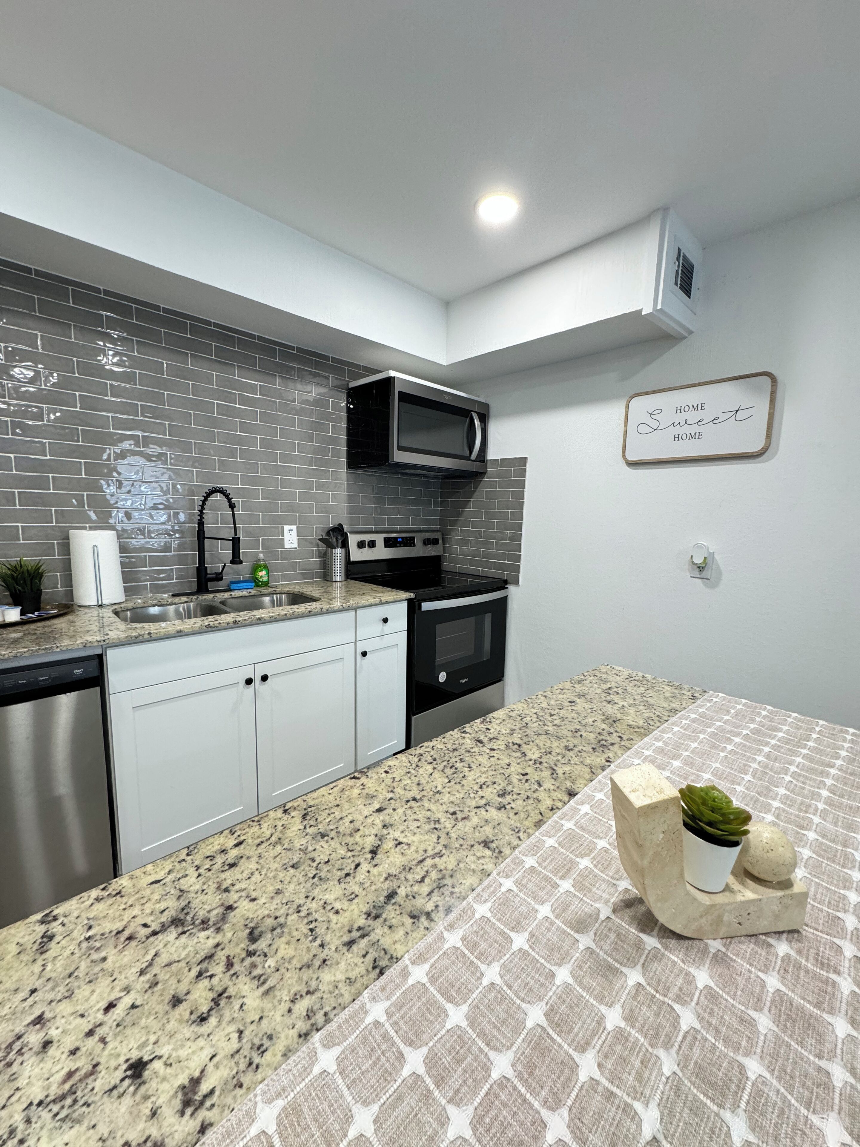 Une cuisine moderne dotée de plans de travail en granit, d’appareils électroménagers en acier inoxydable et d’un revêtement mural en carreaux gris.