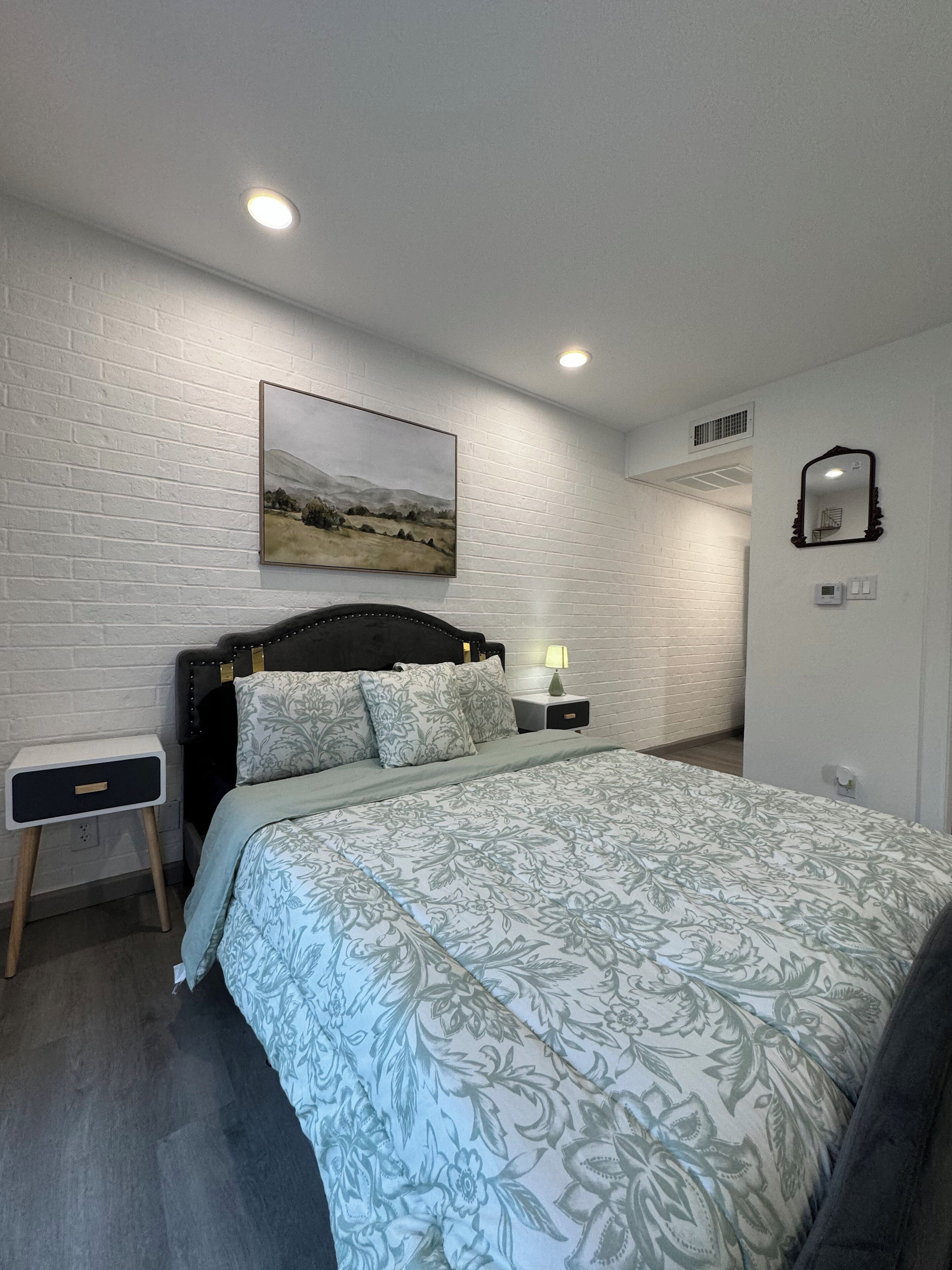 Ein Schlafzimmer mit einem großen Bett, einem Nachttisch, einem wandmontierten Spiegel und einem Gemälde.