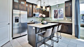 A modern kitchen with dark wood cabinets, stainless steel appliances, and a large island with bar stools. - Entrada at Moab 623 (Moab)